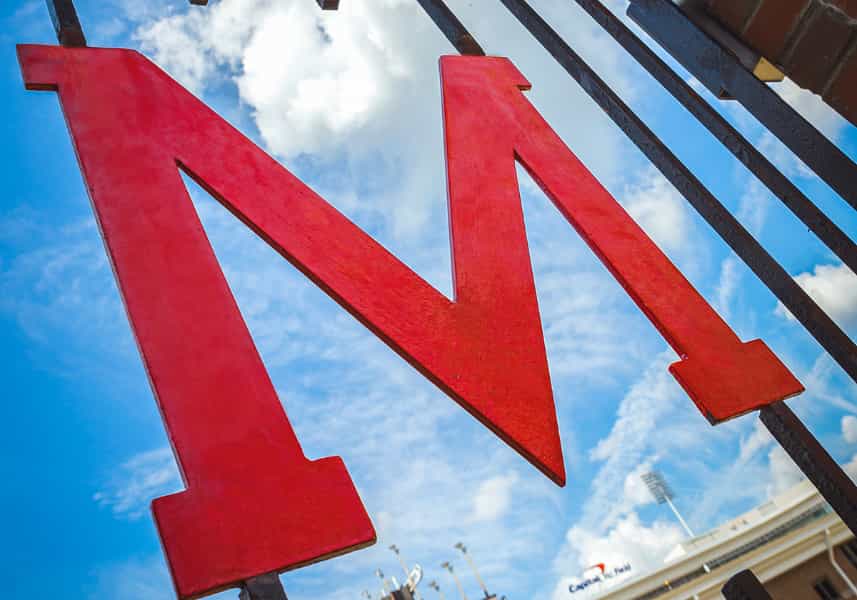 See It, Hear It: Wrought iron red M Gate against brick outside of Maryland Stadium.